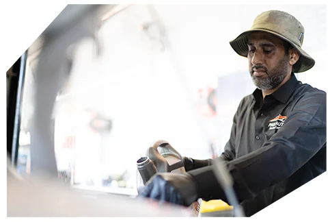 Basic Oil Service02 A mechanic in a gray work shirt and bucket hat focuses intently while performing maintenance work on a vehicle in a garage workshop.