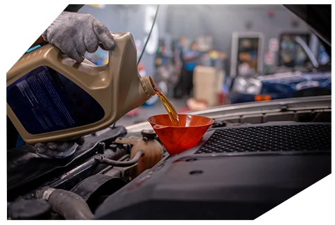 Basic Oil Service05 A gloved hand pours golden-amber motor oil from a tan plastic container into a red funnel positioned in a car's engine compartment during maintenance service.