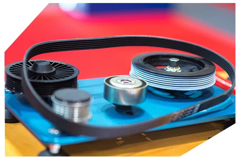 Belts & Hoses06 New serpentine belt with metal pulleys and tensioner displayed on a blue surface against a red background, showing automotive drive components.