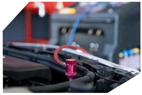 Electrical & Wiring01 Close-up of a car engine compartment showing a metallic pink/red valve cap connected to a service port with diagnostic hoses.