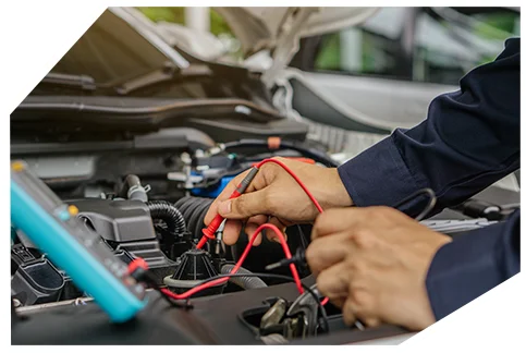 Electrical & Wiring03 Mechanic's hands using red multimeter probes to test electrical components in a vehicle engine bay, wearing navy blue work sleeves.