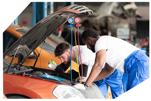 Electrical & Wiring05 Two mechanics working on an orange car with open hood, examining engine while AC pressure gauges with red and blue dials are connected.