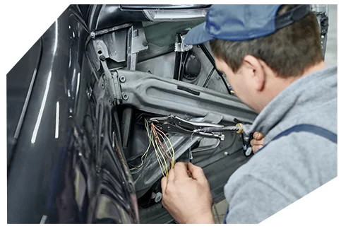 Electrical & Wiring06 Technician in cap examining exposed vehicle wiring and components inside a car door panel that has been removed for repair.