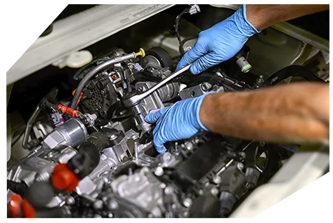 Genaral Automotive 02 A mechanic wearing blue gloves is using a wrench to tighten or loosen a bolt on a car engine, working carefully among various components and hoses.