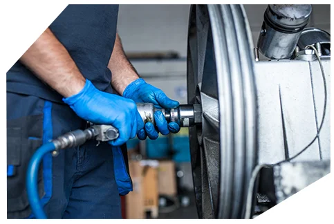 Genaral Automotive 03 A mechanic wearing blue gloves is using a pneumatic impact wrench to tighten or loosen a bolt on a large industrial machine in a workshop setting.