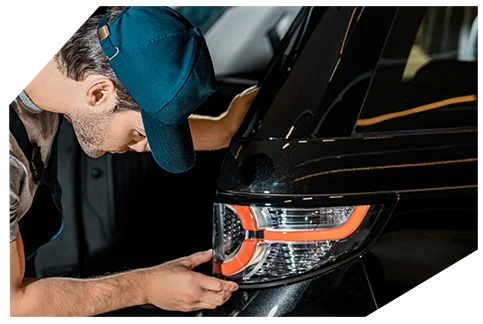 Genaral Automotive 04 A mechanic wearing a cap is carefully inspecting or installing the rear taillight of a black car, ensuring proper alignment and fit in a well-lit workshop.