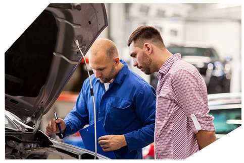 Pink Slip & Registration001 A mechanic in a blue uniform is inspecting a car's engine while discussing the findings with a customer. The mechanic is holding a clipboard and pen and explaining the necessary repairs.