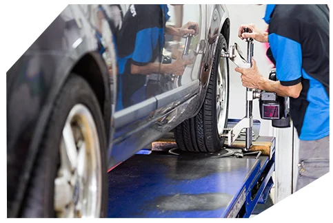 Safety & Tyre Checks02 A mechanic in a blue shirt adjusts a car's wheel alignment on a lift, using a tool on the tire in a garage.