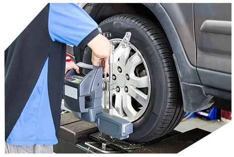 Safety & Tyre Checks03 A mechanic in a blue shirt carefully aligns a car's wheel on a lift, using a precision tool in a busy garage setting with equipment nearby.