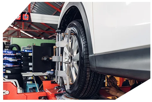 Safety & Tyre Checks04 A white car's wheel is aligned on a lift in a garage, with equipment and tires in the background, using a precision alignment tool.