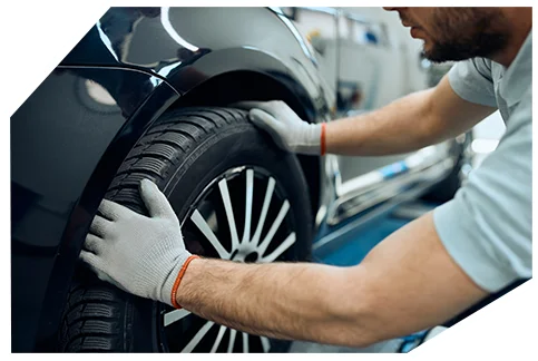 Safety & Tyre Checks05 A mechanic wearing gloves inspects a car's tire on a lift in a garage, ensuring proper alignment with a focus on the wheel and rim.