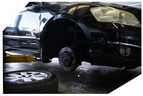 Safety & Tyre Checks06 A black car on a lift in a garage has its wheel removed, exposing the brake disc, with a spare tire resting on the floor nearby.