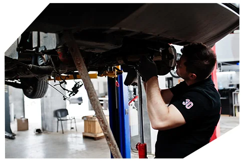 Suspension & Steering06 A mechanic in a black uniform and gloves inspects the undercarriage of a lifted vehicle in a spacious auto repair workshop.