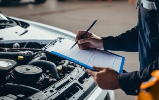 Mechanic filling out inspection checklist in front of an open car hood during pink slip service