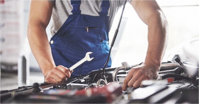 Auto mechanic in blue overalls repairing a car engine with a wrench inside a garage
