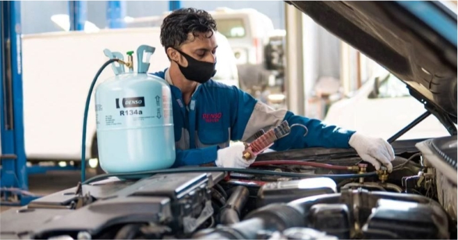 Mechanic performing air conditioning repair and gas refill on a car engine