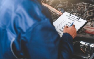 Mechanic checking off items on a vehicle maintenance checklist. Car care and service blog post image