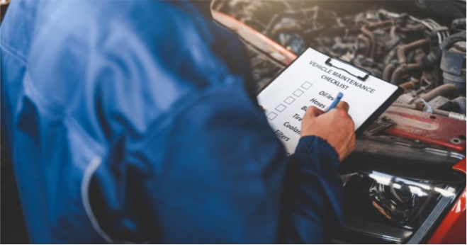 Mechanic checking off items on a vehicle maintenance checklist. Car care and service blog post image