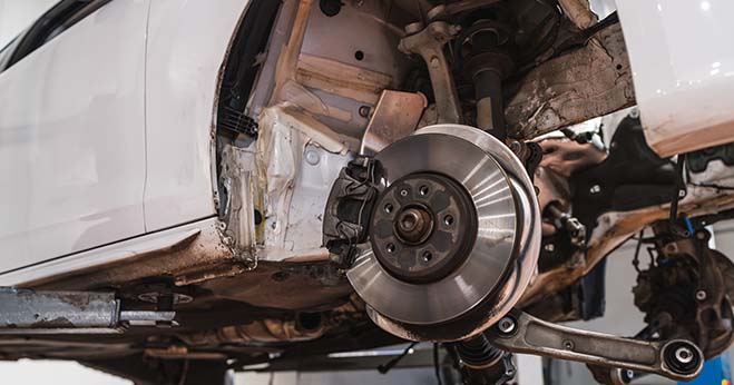 Exposed car suspension system and brake disc assembly on a vehicle lift during a maintenance check.