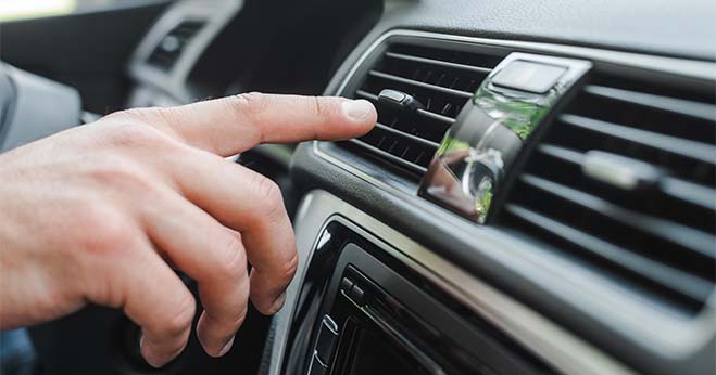 Person adjusting the air conditioning vent inside a modern car dashboard for optimal climate control.