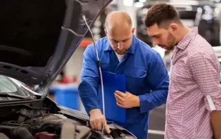 A mechanic in blue overalls showing a car engine to a customer, explaining Hyundai service and repairs for Australian vehicle owners.