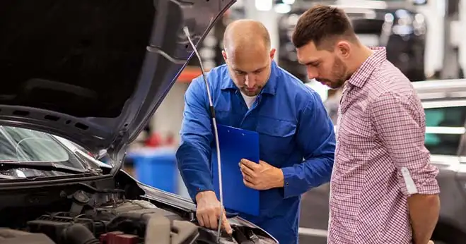 A mechanic in blue overalls showing a car engine to a customer, explaining Hyundai service and repairs for Australian vehicle owners.