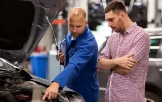 Auto mechanic inspecting car engine belts while explaining replacement signs to customer