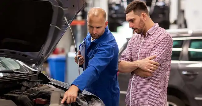Auto mechanic inspecting car engine belts while explaining replacement signs to customer