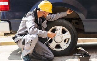 Mechanic inspecting a car wheel and braking system with tools, demonstrating parking brake or emergency brake maintenance