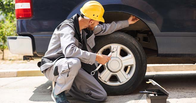 Mechanic inspecting a car wheel and braking system with tools, demonstrating parking brake or emergency brake maintenance