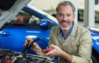 auto electrician testing car battery with diagnostic tool inside workshop