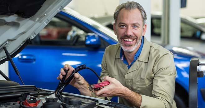 auto electrician testing car battery with diagnostic tool inside workshop