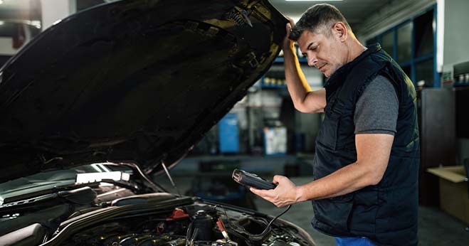 mechanic inspecting car engine with diagnostic tool after check engine light warning